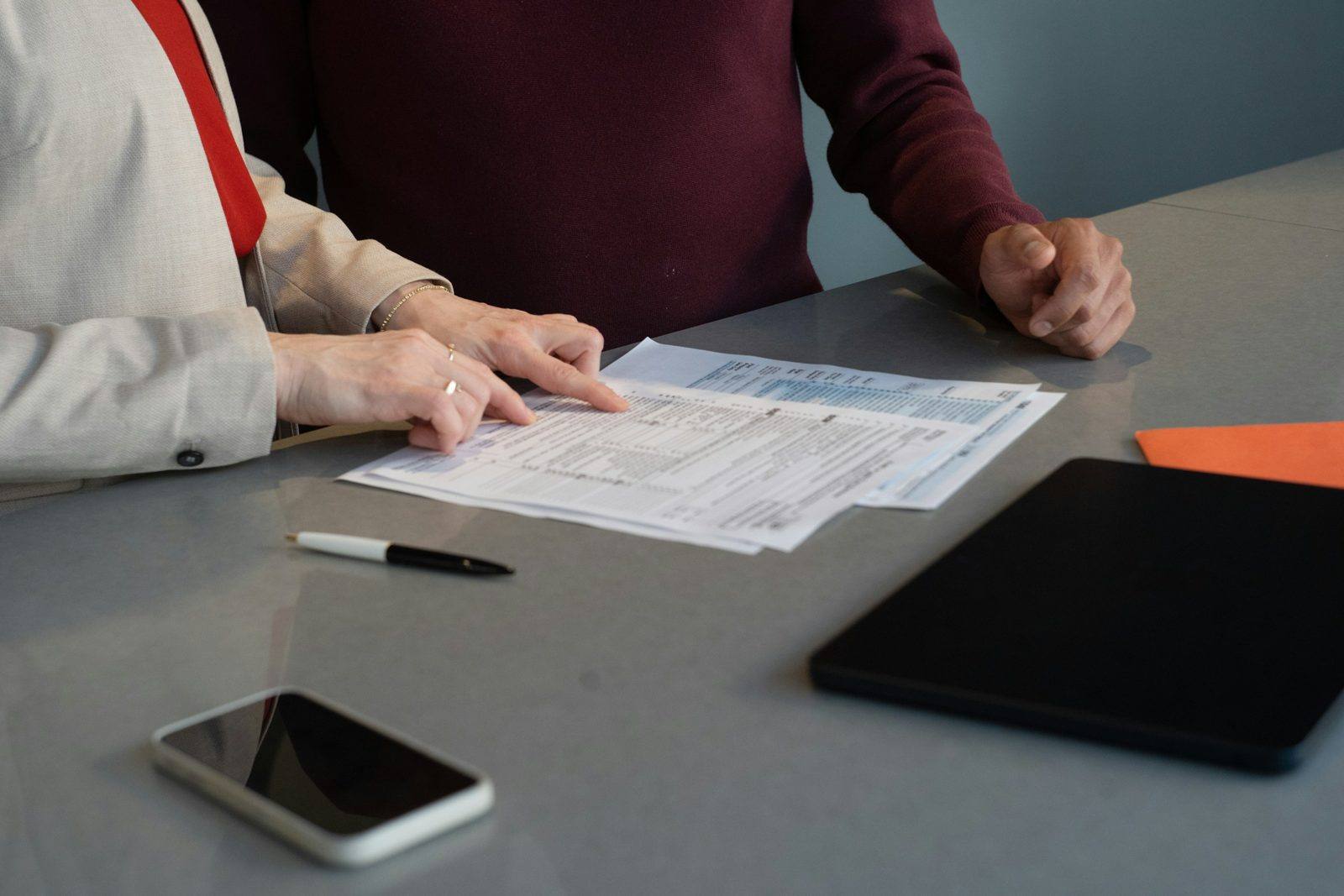 Two people at a table going over printed financial paperwork, a pen and phone beside them